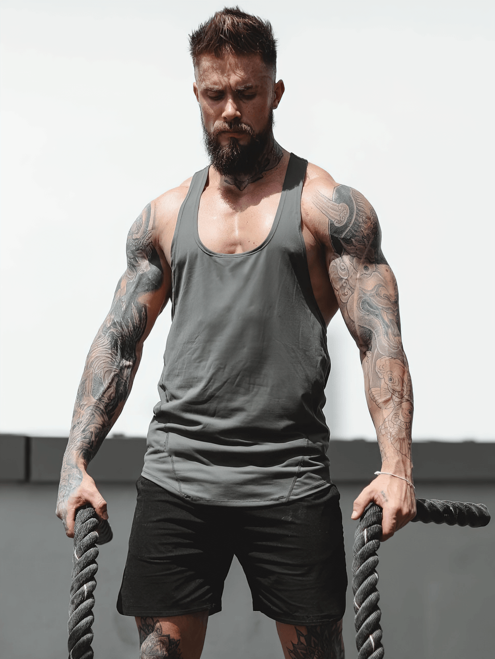 Man wearing Elastic Stringer Tank Top for Bodybuilding Training - SF4167 during intense workout with ropes, showcasing muscles.