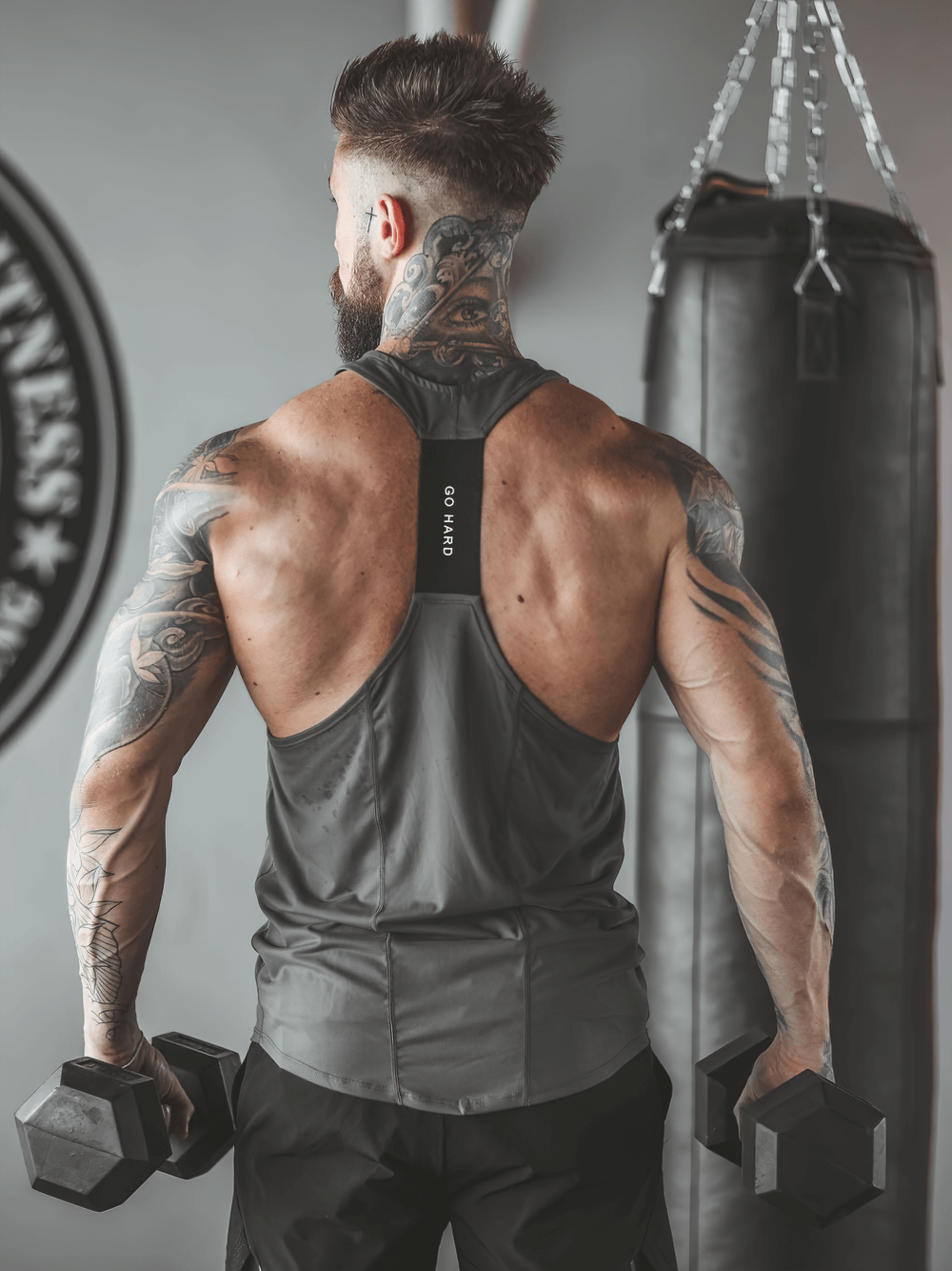 Back view of a man wearing an Elastic Stringer Tank Top for Bodybuilding Training - SF4167, lifting dumbbells in a gym.