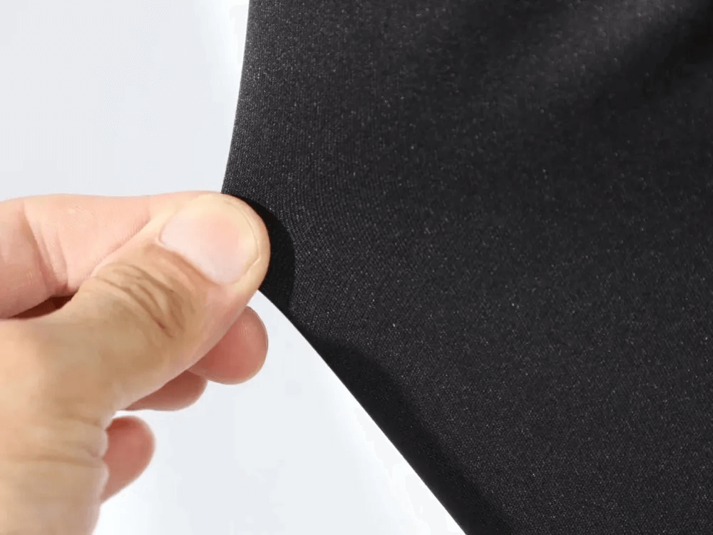Close-up of hand stretching elastic fabric of men's training pants, showcasing durability and flexibility.