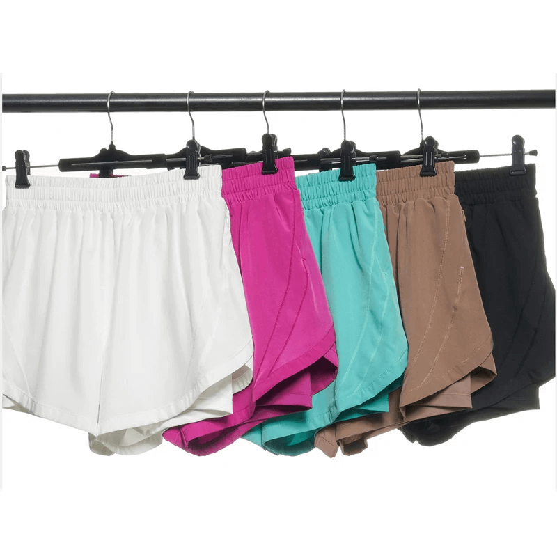 Colorful elastic waist shorts for active wear displayed on a hanger, showcasing white, pink, teal, beige, and black options.