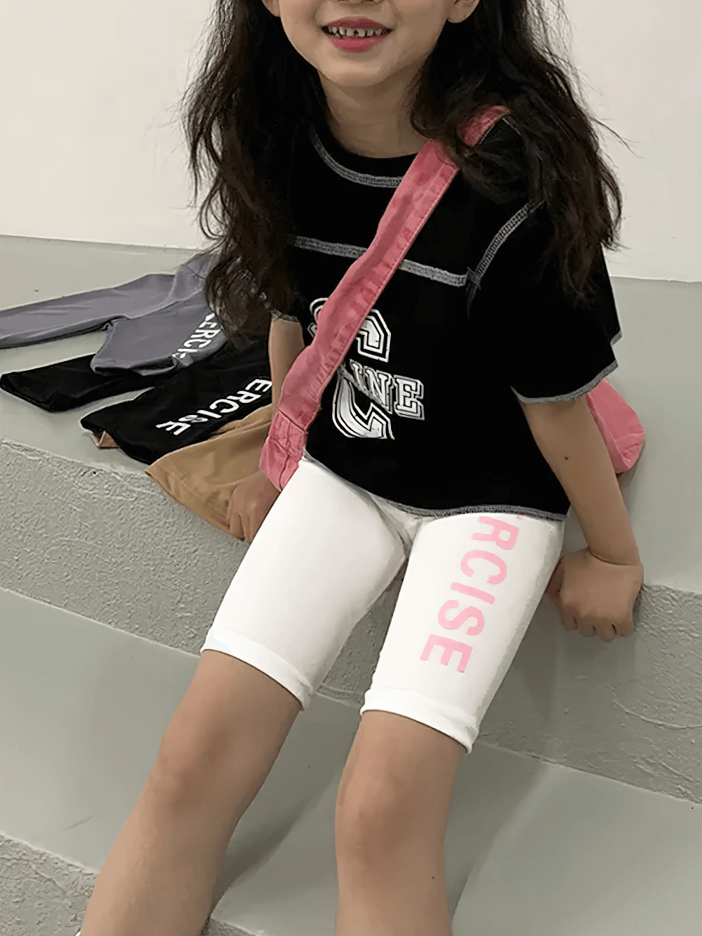 Girl wearing Exercise Print Stretch Biker Shorts for Active Wear - SF3758, sitting on stairs with playful smile and pink shoulder bag.