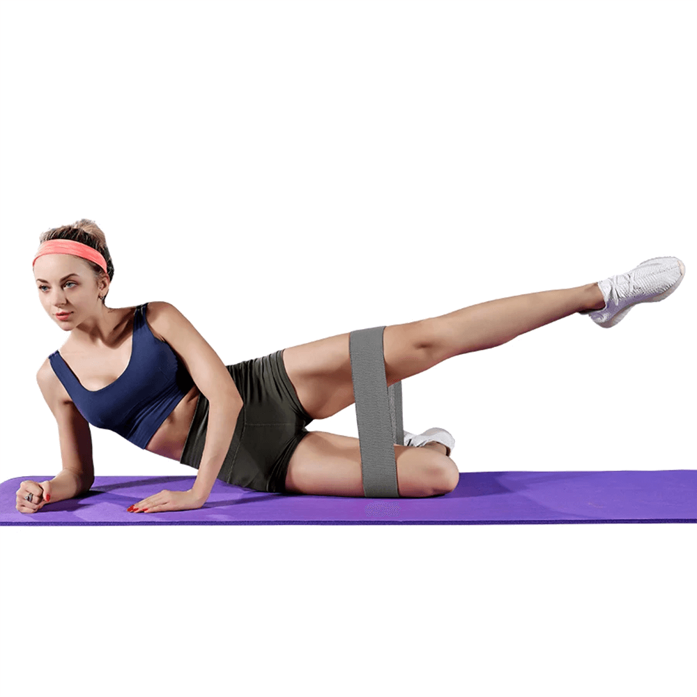 Woman exercising with fabric resistance hip band on yoga mat, demonstrating glute and thigh workout.