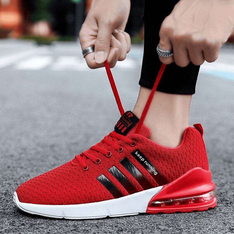 Person tying red breathable lightweight men's running sneakers with cushioning and flexible technology on pavement.
