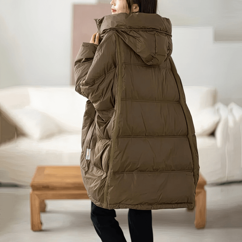 Woman wearing oversized brown down jacket with hood in cozy living room