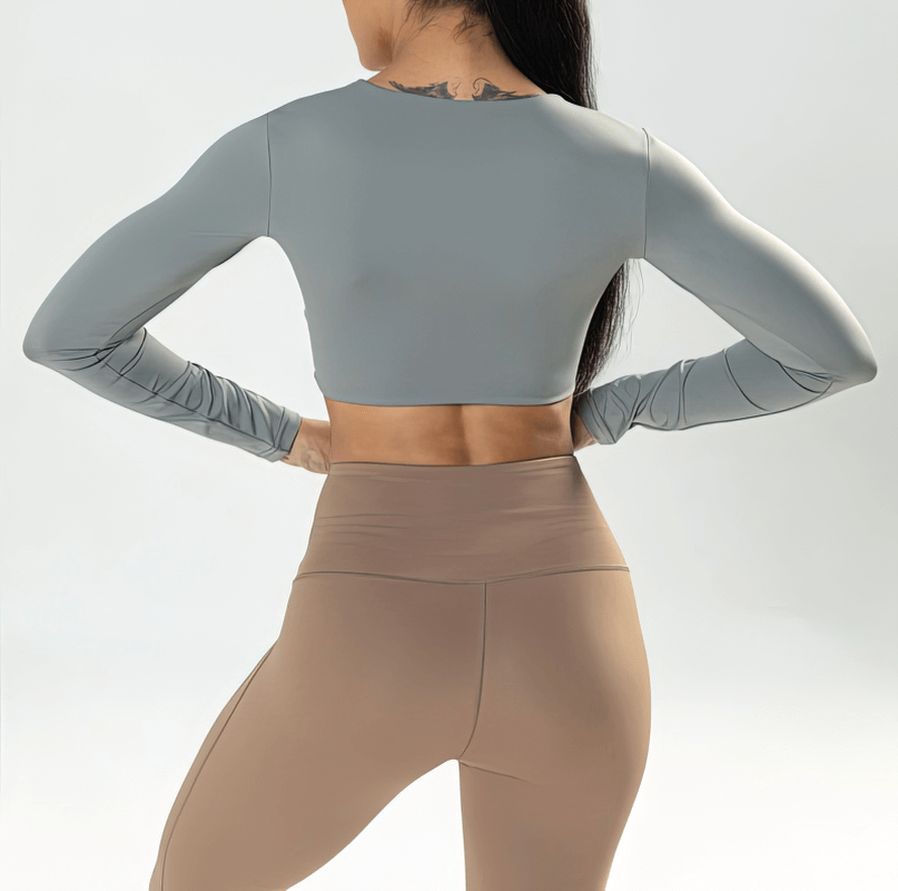 Back view of woman in grey cropped sporty long sleeve top, nylon-spandex blend for workouts; stylish and breathable activewear.