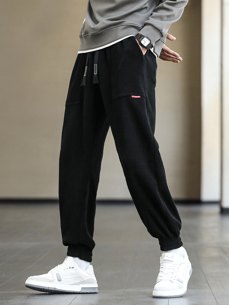 Stylish men's black corduroy sweatpants with elastic hem and drawstring closure, paired with white sneakers for casual fashion.