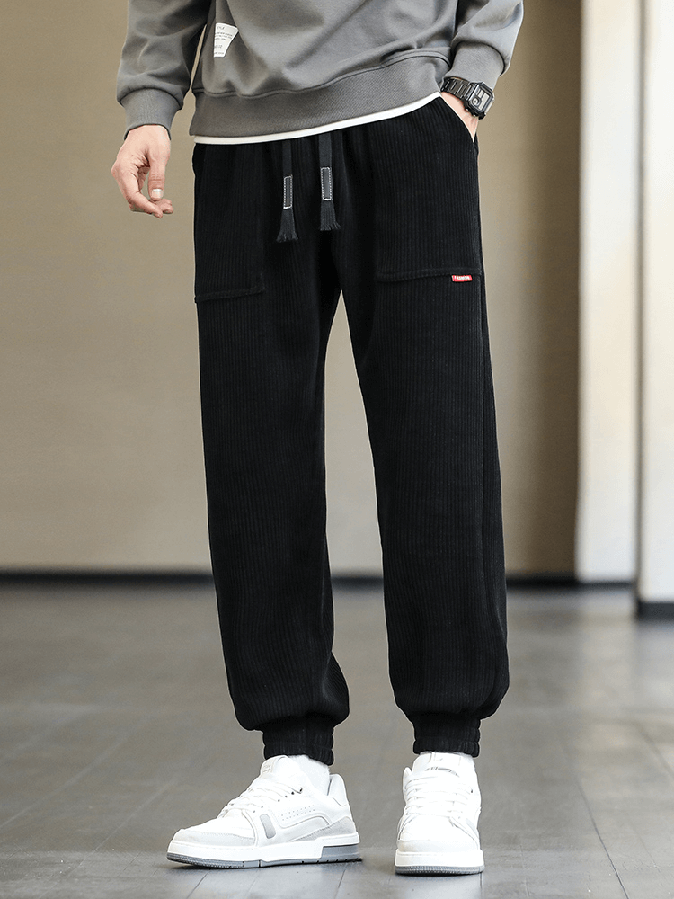 Man wearing black fashion corduroy sweatpants with elastic hem, paired with white sneakers, showcasing stylish loose casual joggers.
