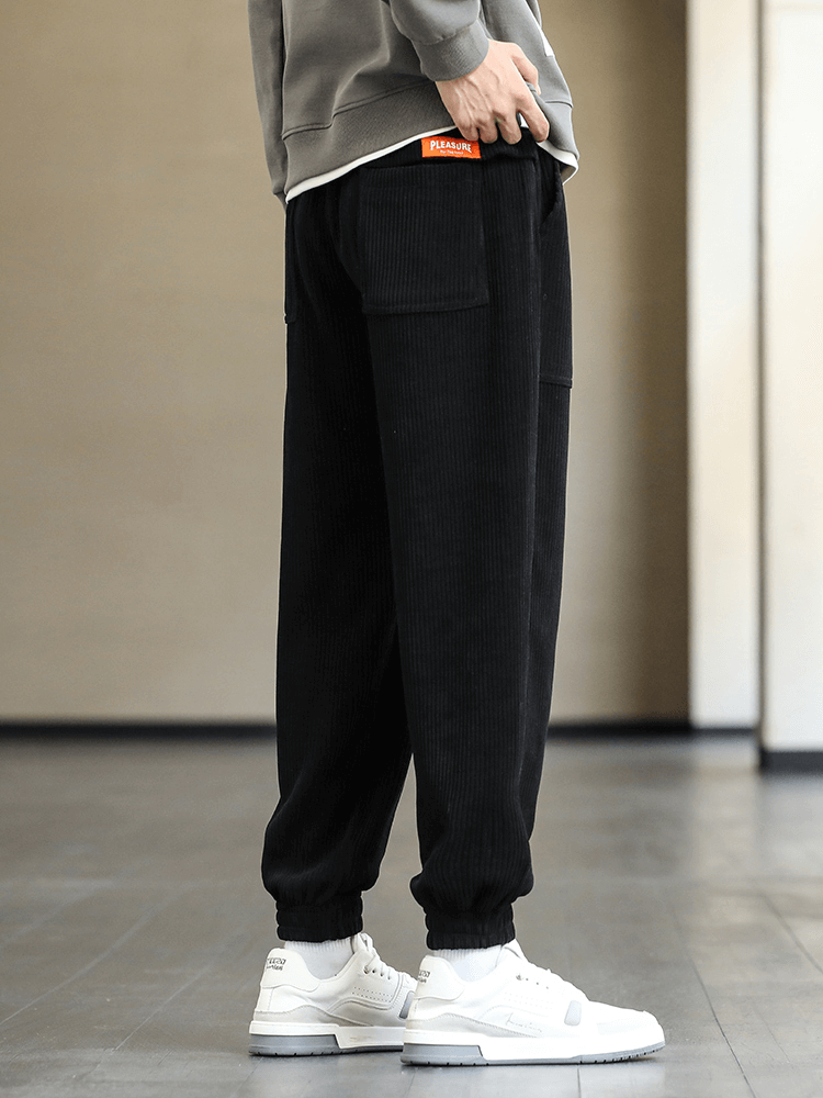 Man wearing black corduroy sweatpants with elastic hem and white sneakers, showcasing stylish and comfortable fit. SF1410 model.