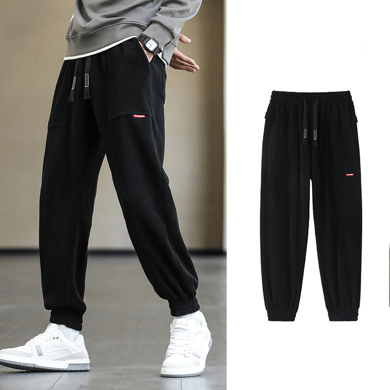 Stylish black corduroy sweatpants with elastic hem, perfect for men seeking loose casual joggers. Model wearing with white sneakers.