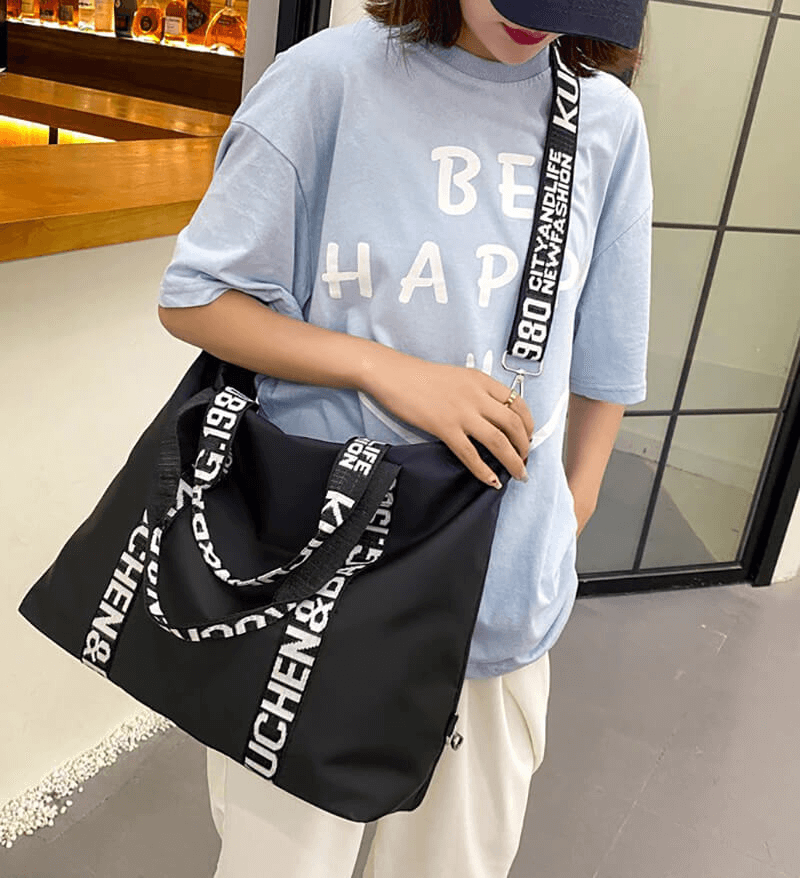 Stylish black nylon women's yoga handbag with white lettering strap, worn by a model in a casual blue T-shirt.