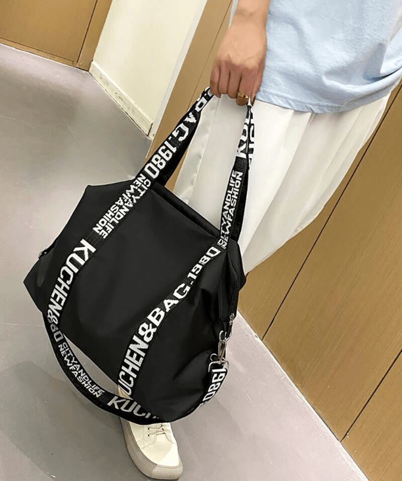 Person holding a black lightweight yoga handbag with white lettered straps, perfect for gym and travel, available in multiple colors.