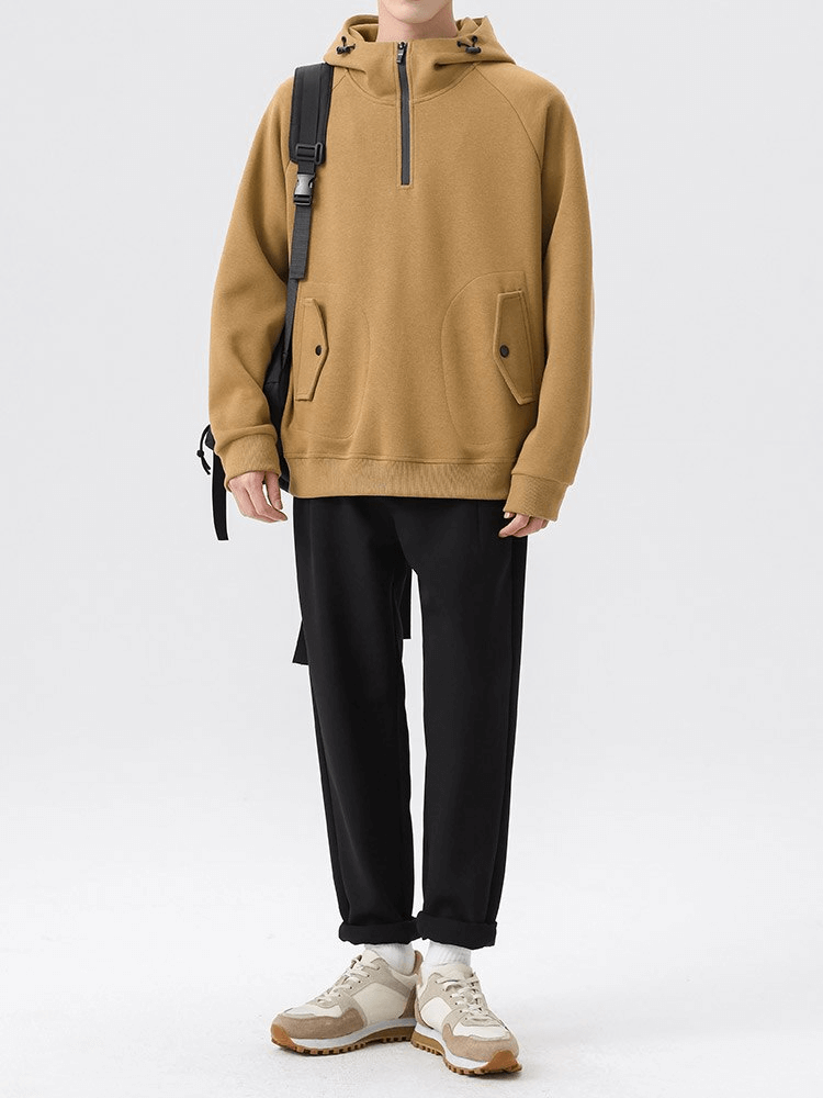 Men's khaki half-zip hoodie with pockets, worn with black pants and white sneakers for a casual look.
