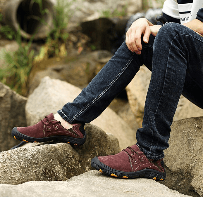 Man wearing burgundy genuine leather shoes for outdoor trekking, seated on rocks showcasing stylish breathable footwear with rubber outsole.