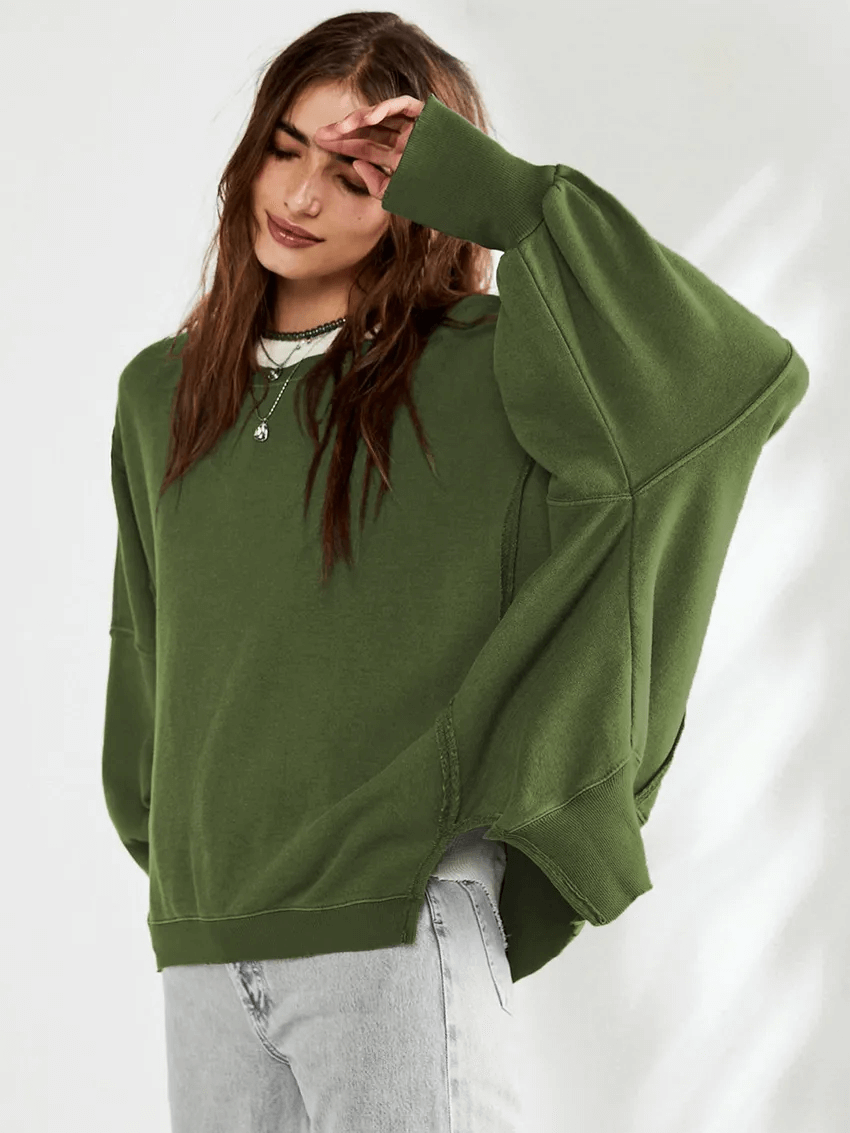 Woman wearing green drop-shoulder loose sweatshirt with O-neck and three-quarter sleeves, styled casually with jeans.