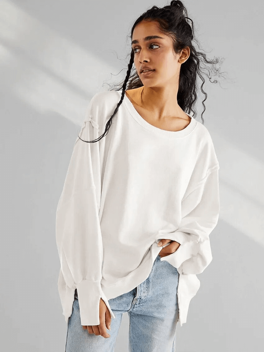 Woman wearing a white drop-shoulder loose sweatshirt with O-neck and three-quarter sleeves, paired with jeans, showcasing casual fashion.
