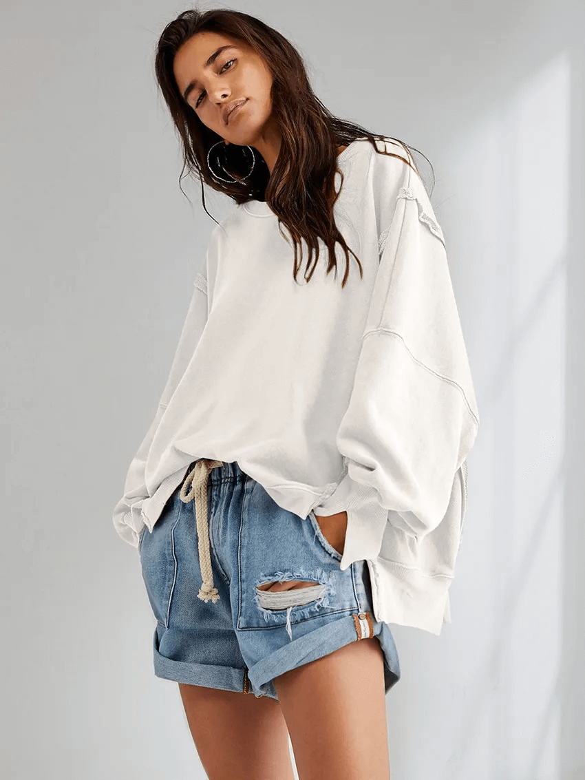 Woman in solid color drop shoulder loose sweatshirt with denim shorts, casual fashion style.