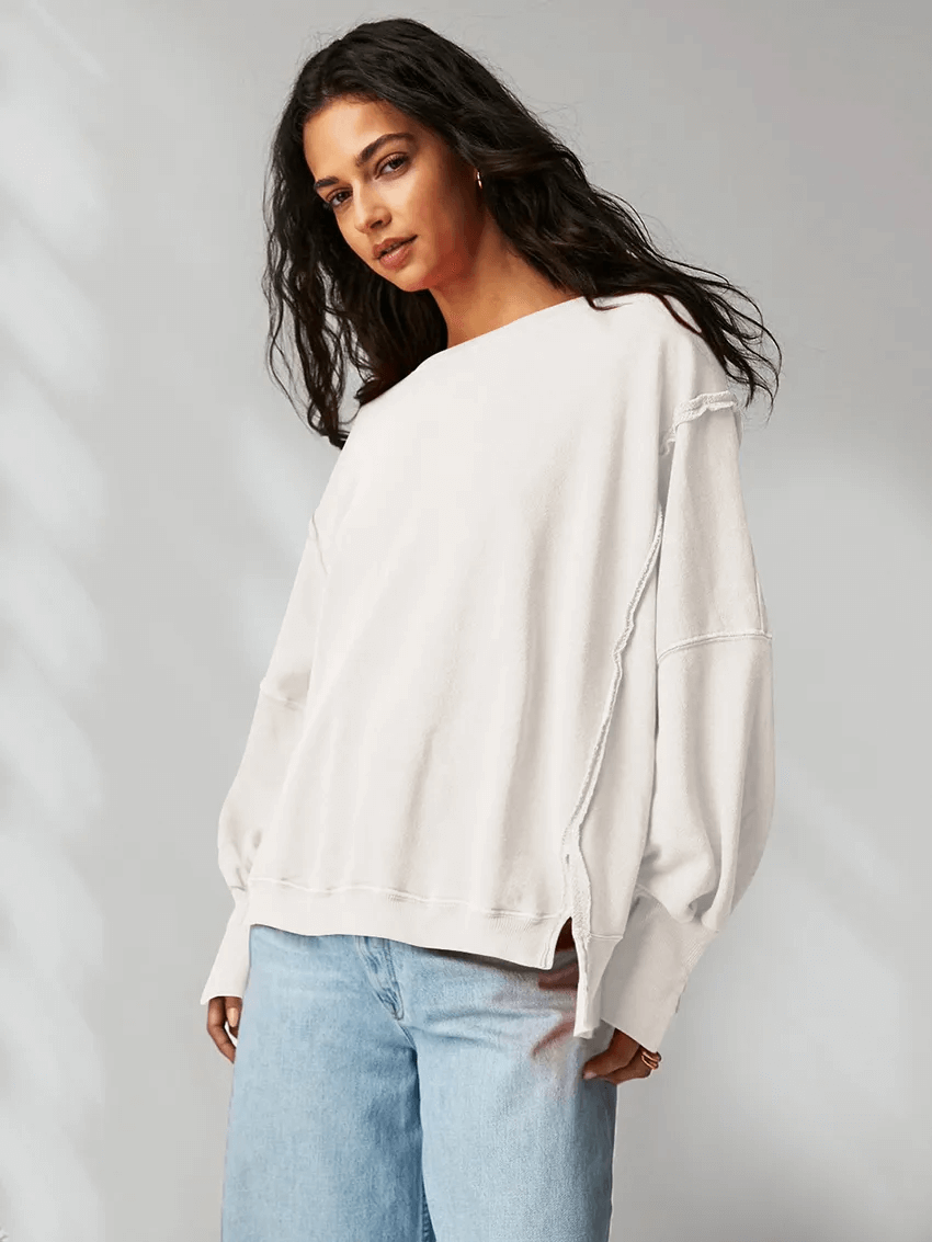 Woman wearing loose fit white drop shoulder sweatshirt and jeans, stylish casual outfit with O-neck and three-quarter sleeves.