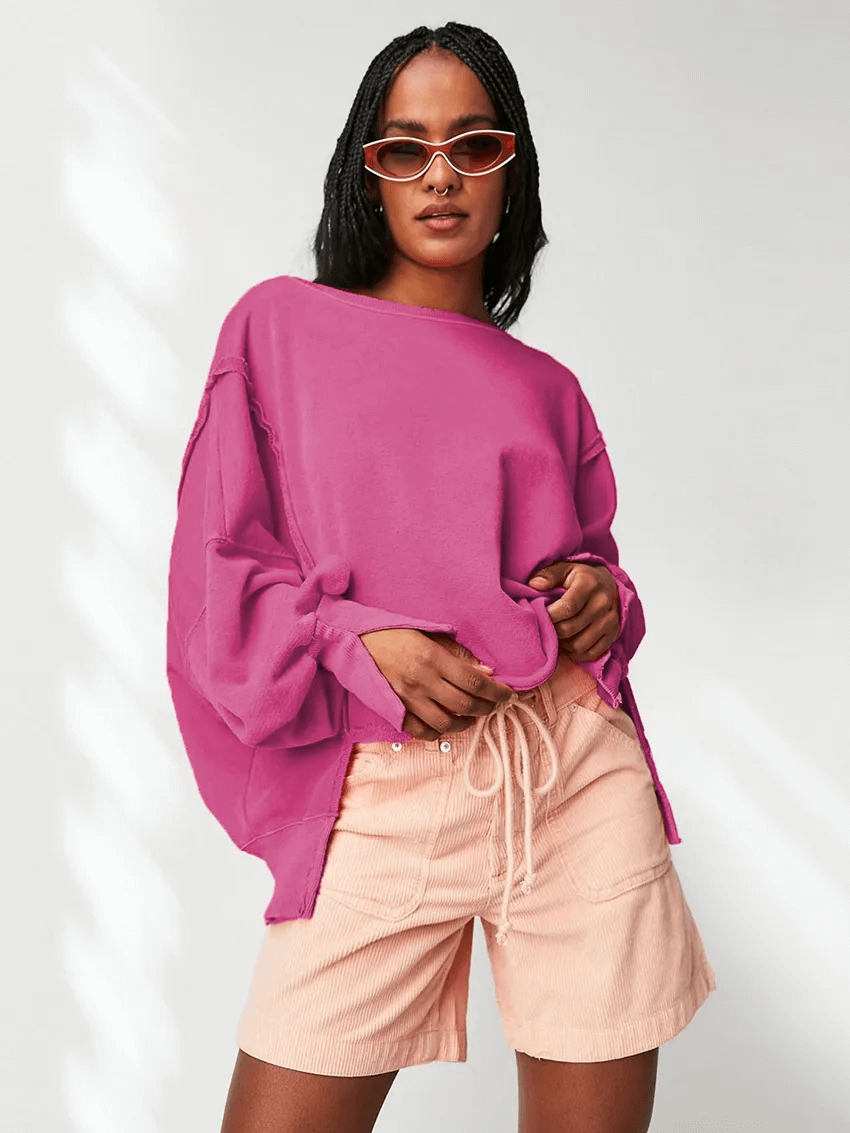 Woman wearing loose pink drop shoulder sweatshirt with peach shorts, featuring O-neck collar and unique style for a casual look.