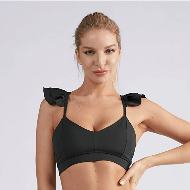 Woman wearing black solid color elastic sports bra for fitness activities like yoga and running. Nylon fabric ensures comfort and coverage.