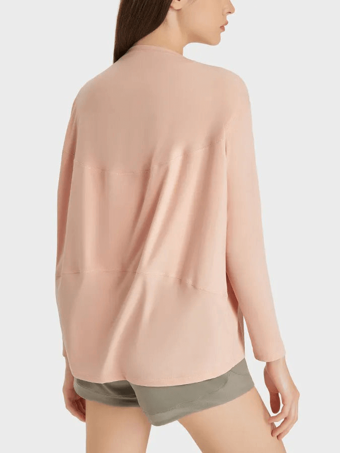 Woman wearing a pink long sleeve loose top for gym, showing the back view, made from durable nylon and spandex blend, paired with shorts.