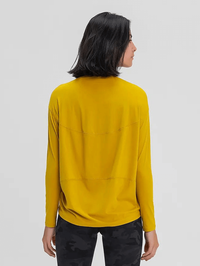 Back view of a woman wearing a yellow long-sleeved gym top, loose fit, made of breathable fabric, paired with black patterned leggings.