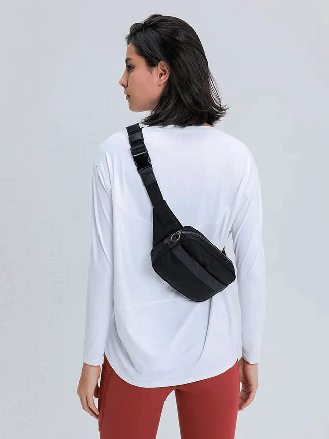 Woman wearing white long-sleeve gym top, black crossbody bag, and red leggings