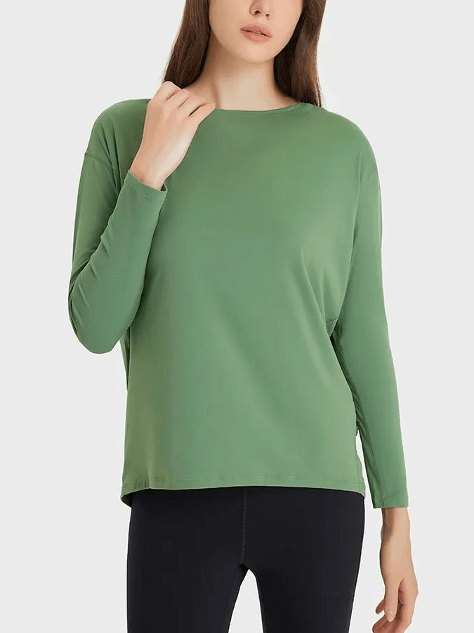 Woman wearing a green, long-sleeved loose top for gym made of durable nylon and spandex, paired with black pants, ideal for workouts.