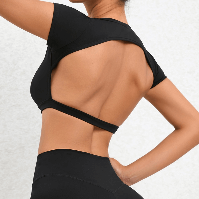 Back view of a fashionable elastic women's cropped top with an open back, perfect for yoga. Short sleeves, nylon material, in black.