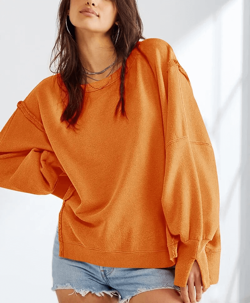 Woman wearing an oversized orange sweatshirt with reversible seam and loose fit, perfect for elegant and casual style.