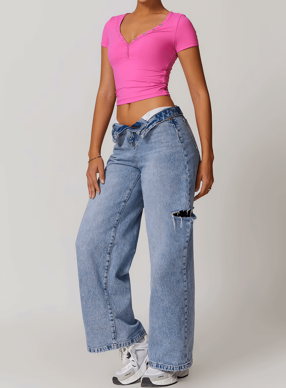 Woman wearing a pink V-neck crop top with short sleeves paired with high-waisted baggy jeans and white sneakers.
