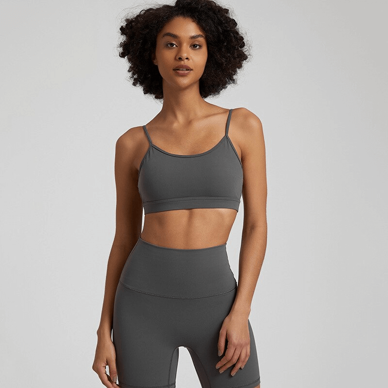 Female model wearing a gray solid color open back sports bra, perfect for workout comfort and breathability, paired with matching activewear.