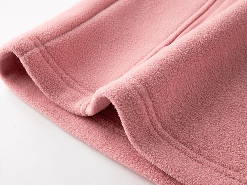 Close-up of pink fleece fabric from a women's stand collar zip-up jacket with pockets, showcasing texture and craftsmanship.