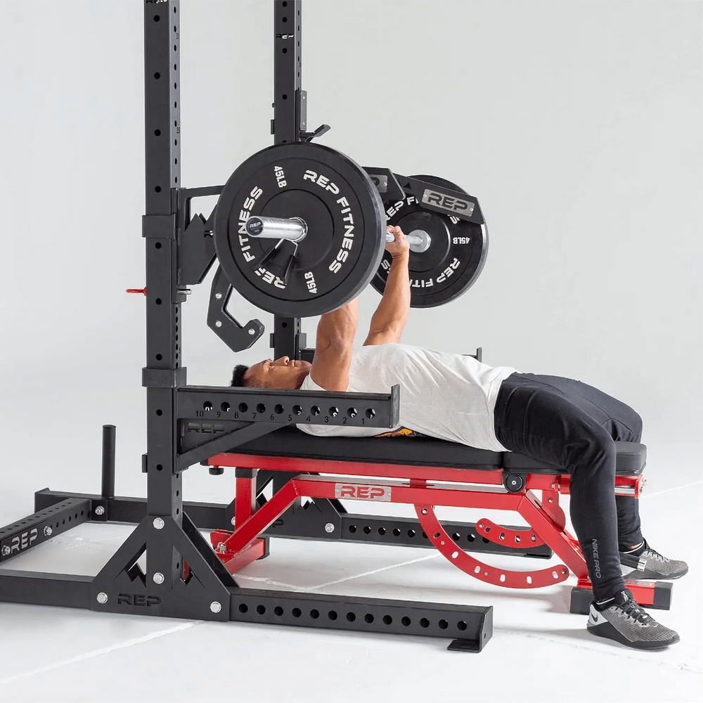 Man lifting REP Fitness bumper plates on bench press in gym setup