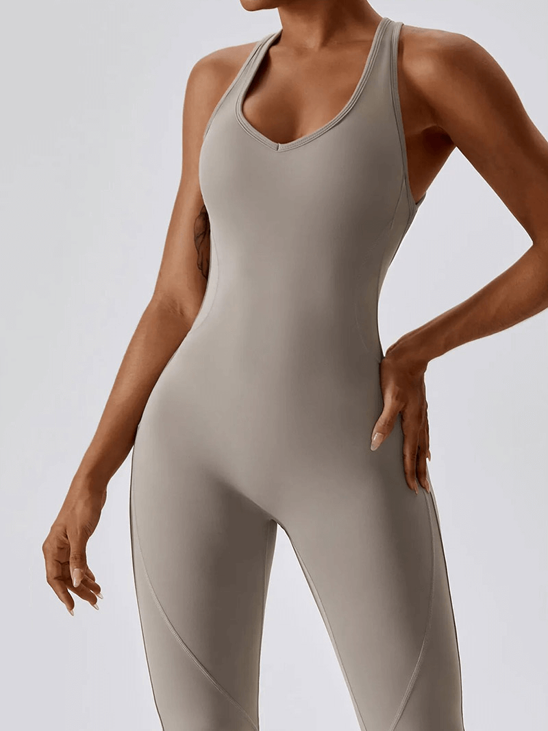 Woman wearing a fitness open back compressed jumpsuit in grey, ideal for yoga, running, and gym activities, featuring quick-dry fabric.