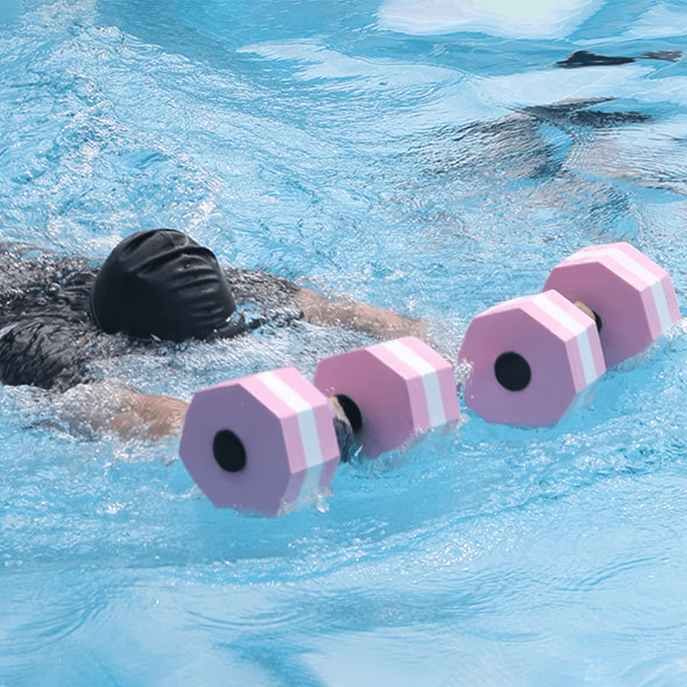 Person using pink foam floating dumbbells in pool for water fitness training, aiding in low-impact exercise.
