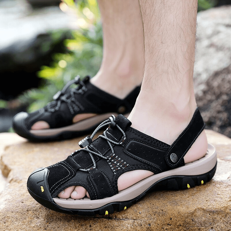 Man wearing genuine leather men's sandals with removable buckle, enjoying a walk on rocks. Durable and stylish footwear.