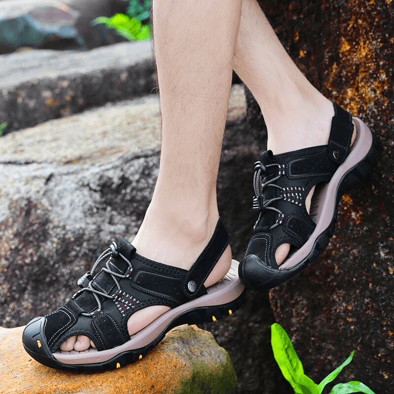Men's soft leather sandals with removable buckle, black color, worn outdoors on rocky terrain for comfort and style.