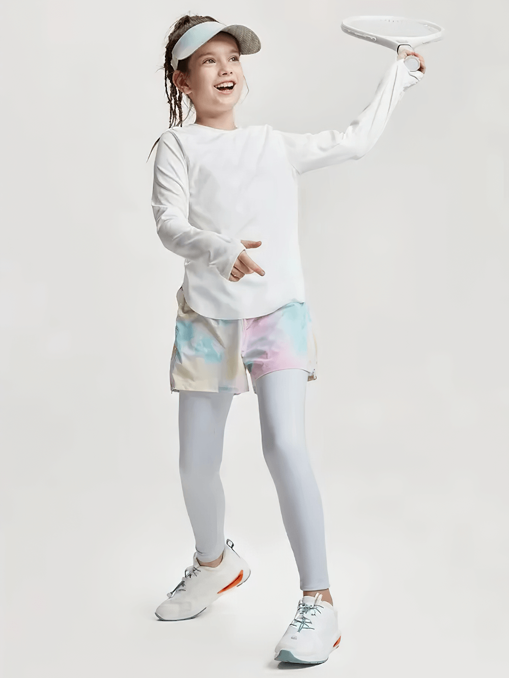 Girl playing wearing white sports top and pastel shorts, smiling, showing active lifestyle. Ideal for promoting girls athletic wear.