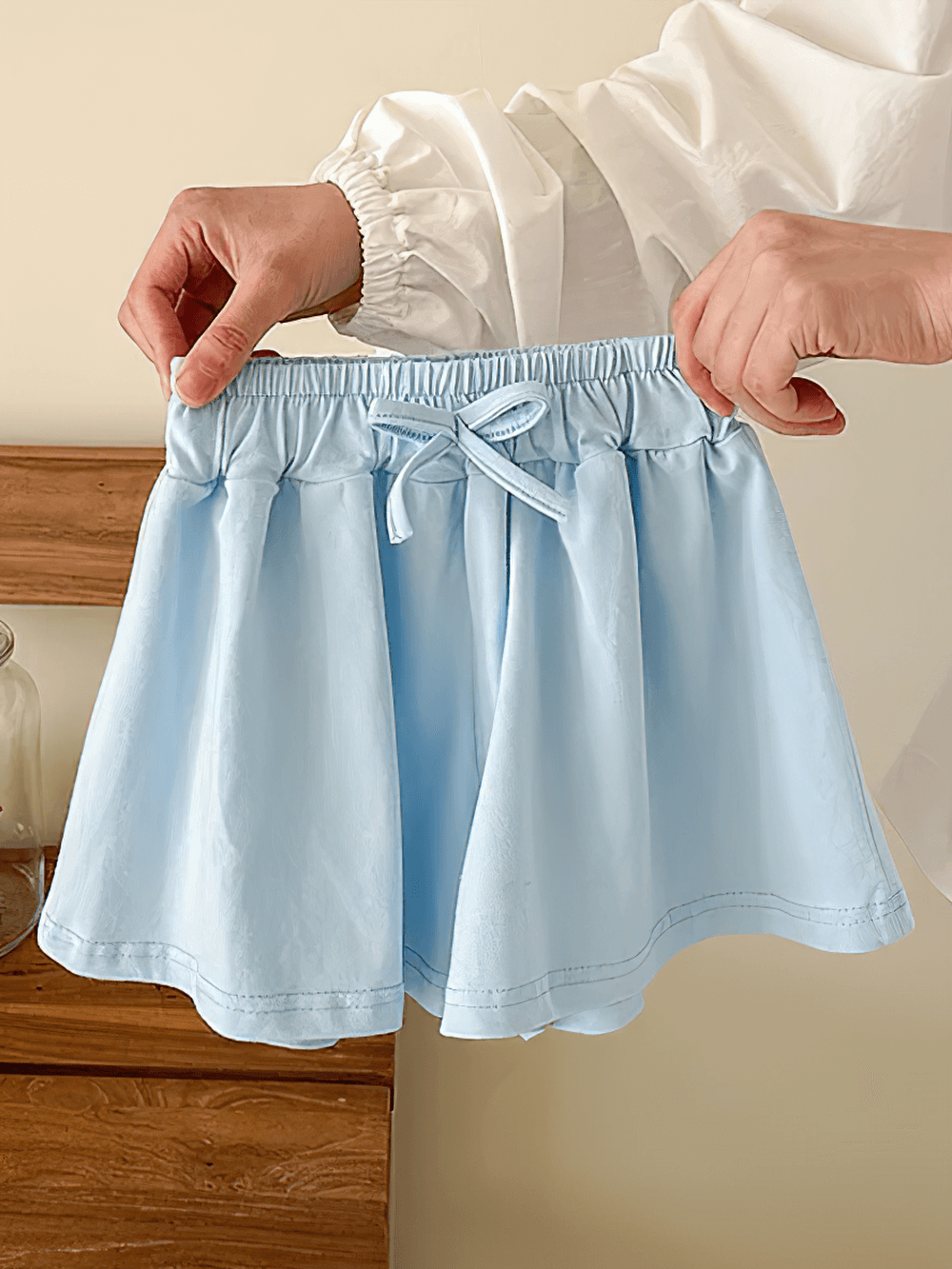 Hands holding Girls' Soft Cotton Drawstring Loose Shorts - SF3737 in light blue, showcasing a relaxed silhouette and stretchy waistband.