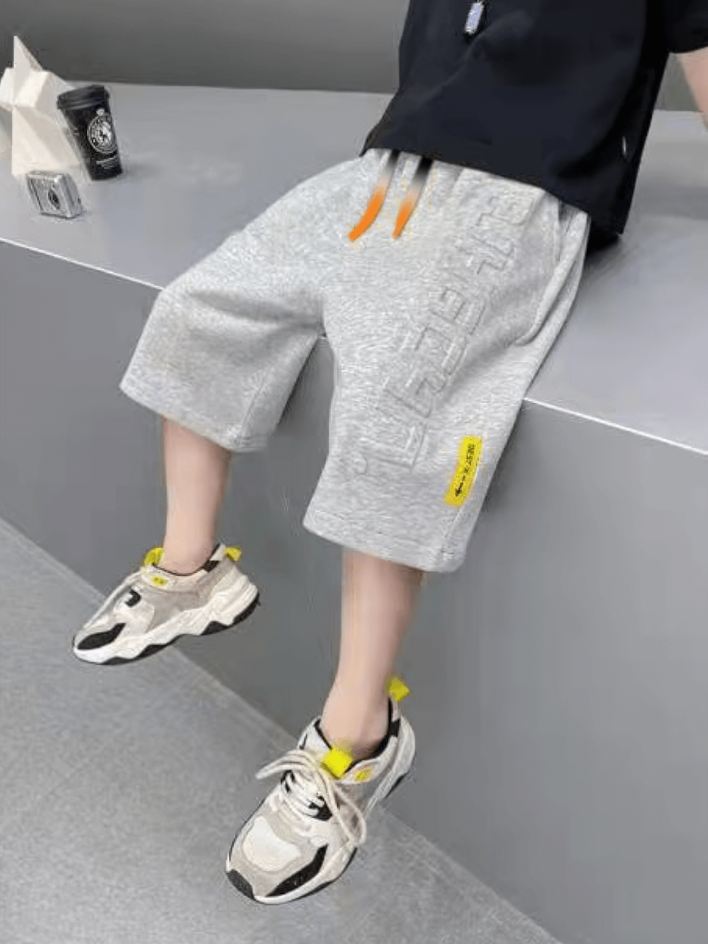 Child wearing Graphic Drawstring Knee-Length Sports Shorts - SF3771, featuring a trendy print and drawstring waist, sitting on a ledge.