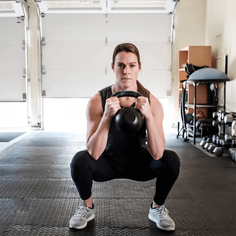 Person doing kettlebell squat on EVA foam gym floor mats in a home gym setup.