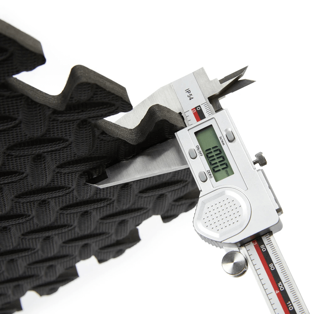 Close-up of caliper measuring thickness of black EVA foam gym mat tile, showing interlocking design for home gym flooring.