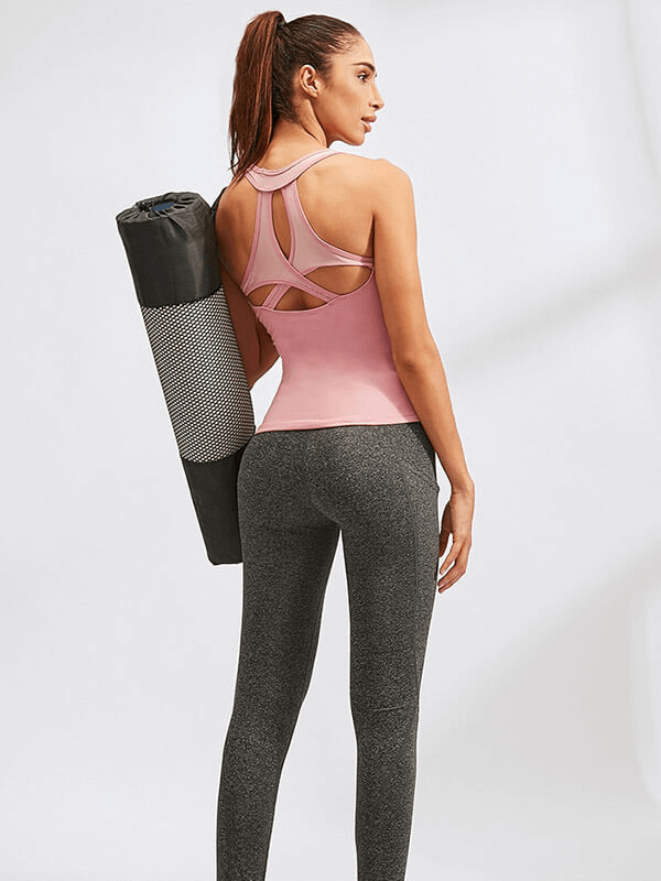 Woman in pink asymmetric back yoga tank holding a rolled mat, showcasing breathable sportswear ideal for yoga and fitness activities.