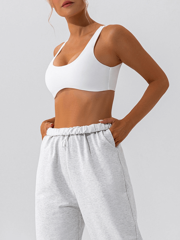 Woman wearing white seamless gym workout sports bra and gray joggers, showcasing breathable design and comfort. Ideal for yoga and fitness.
