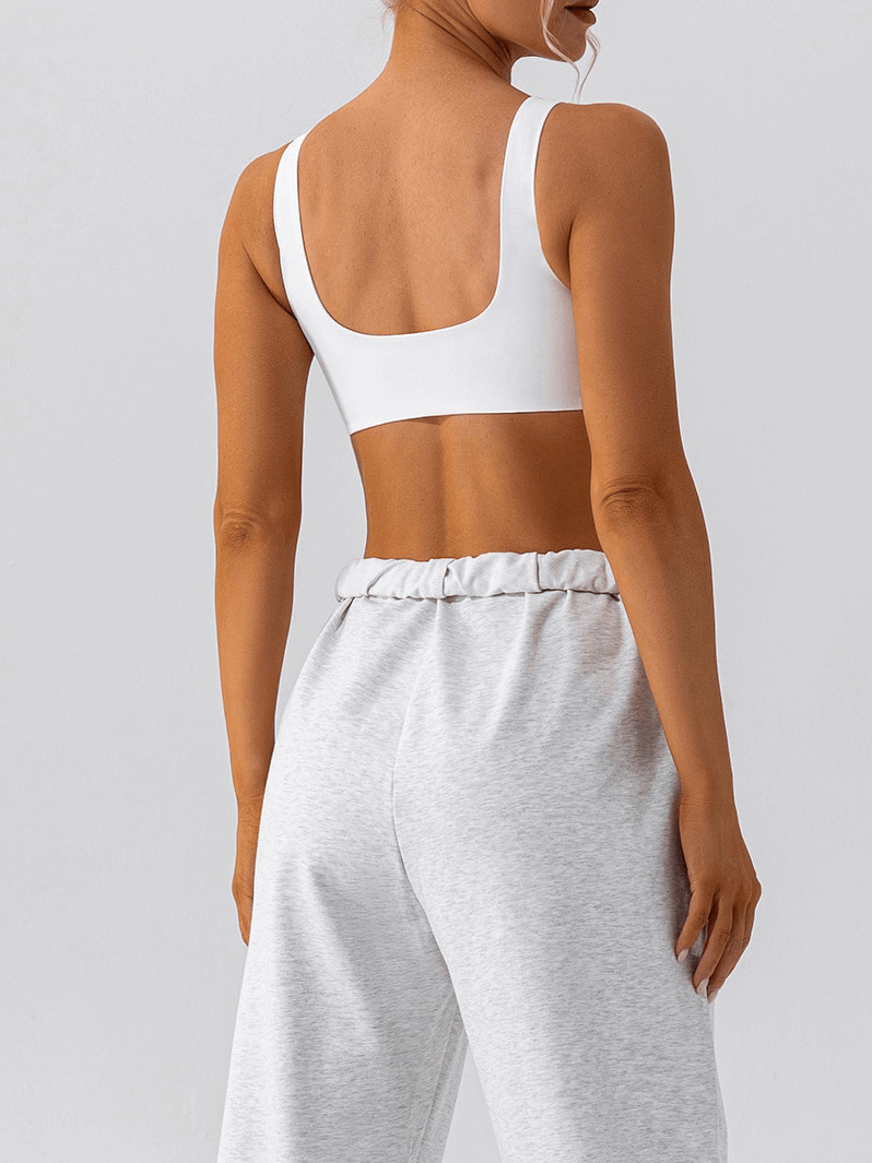 Back view of a woman in a white breathable seamless sports bra and gray pants, designed for comfort during workouts and yoga.