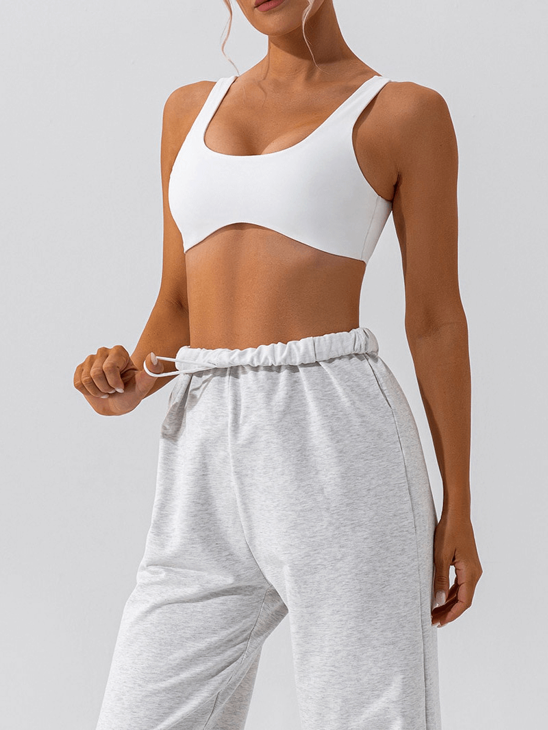 Woman in white seamless sports bra and gray sweatpants ready for yoga; gym workout breathable soft underwear