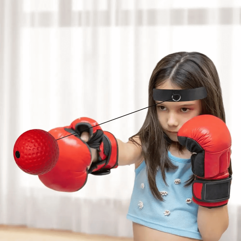 Young girl practicing with a headband boxing reflex ball, enhancing hand-eye coordination and reflexes with red gloves and PU punch ball.