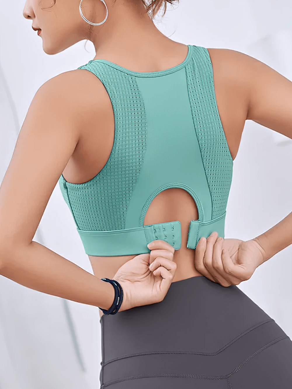 Woman adjusting teal high-impact sports bra with quick-dry fabric, showcasing back design and fixed pad support for gym workouts.