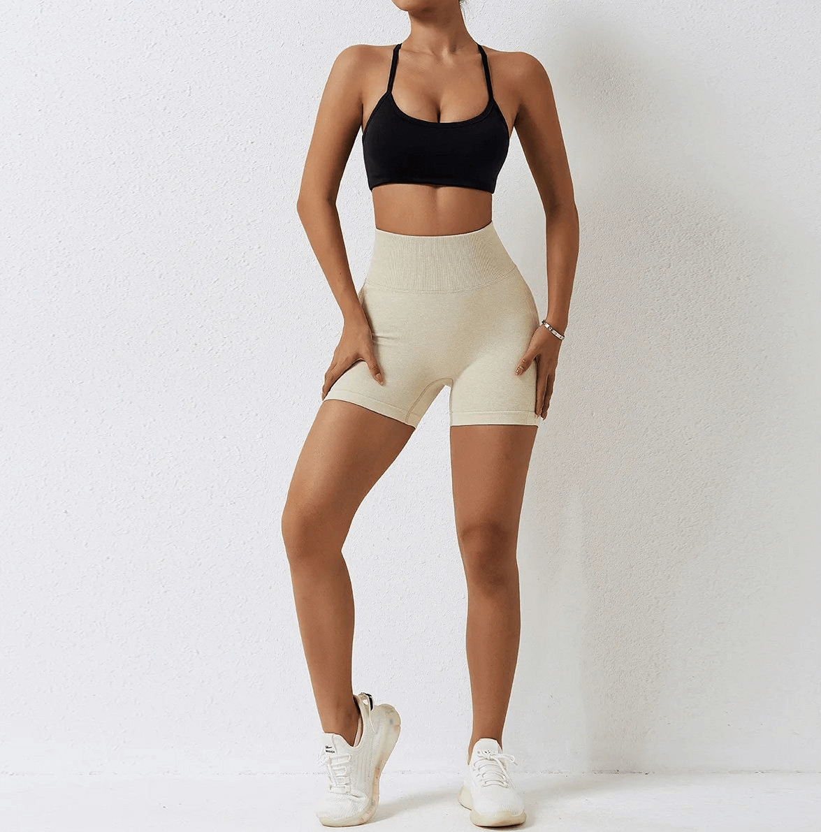 Woman wearing beige nylon spandex yoga shorts and black sports bra, showcasing workout apparel for high-impact activities.