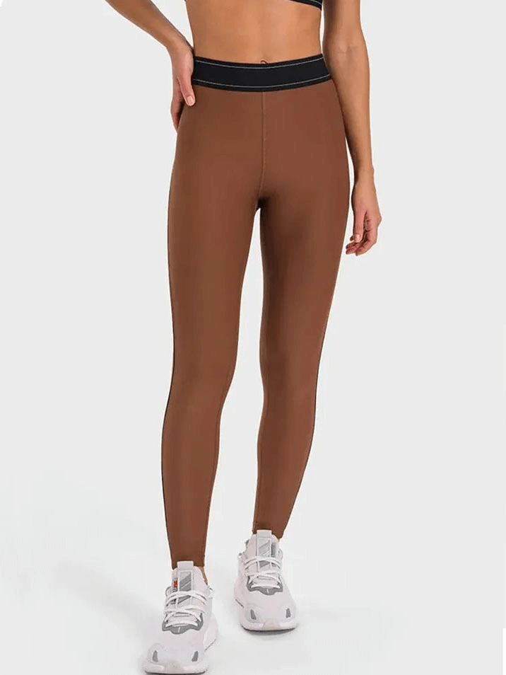 High-waisted brown gym compression leggings with elastic waist, perfect for yoga and running, paired with white sneakers.